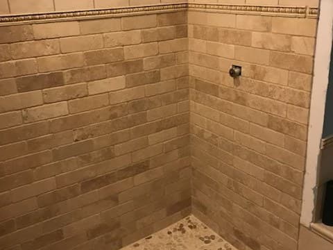 A rebuilt shower finished in stacked stone tile with a pebble floor