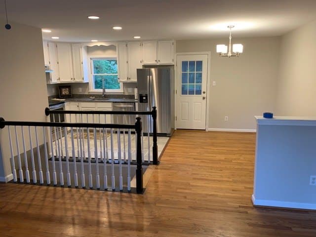 A finished stair opening with new white balusters and a black handrail, beside a refinished hardwood floor