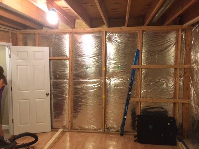 A basement wall stripped to the studs with foil insulation between the framing, an interior door already hung